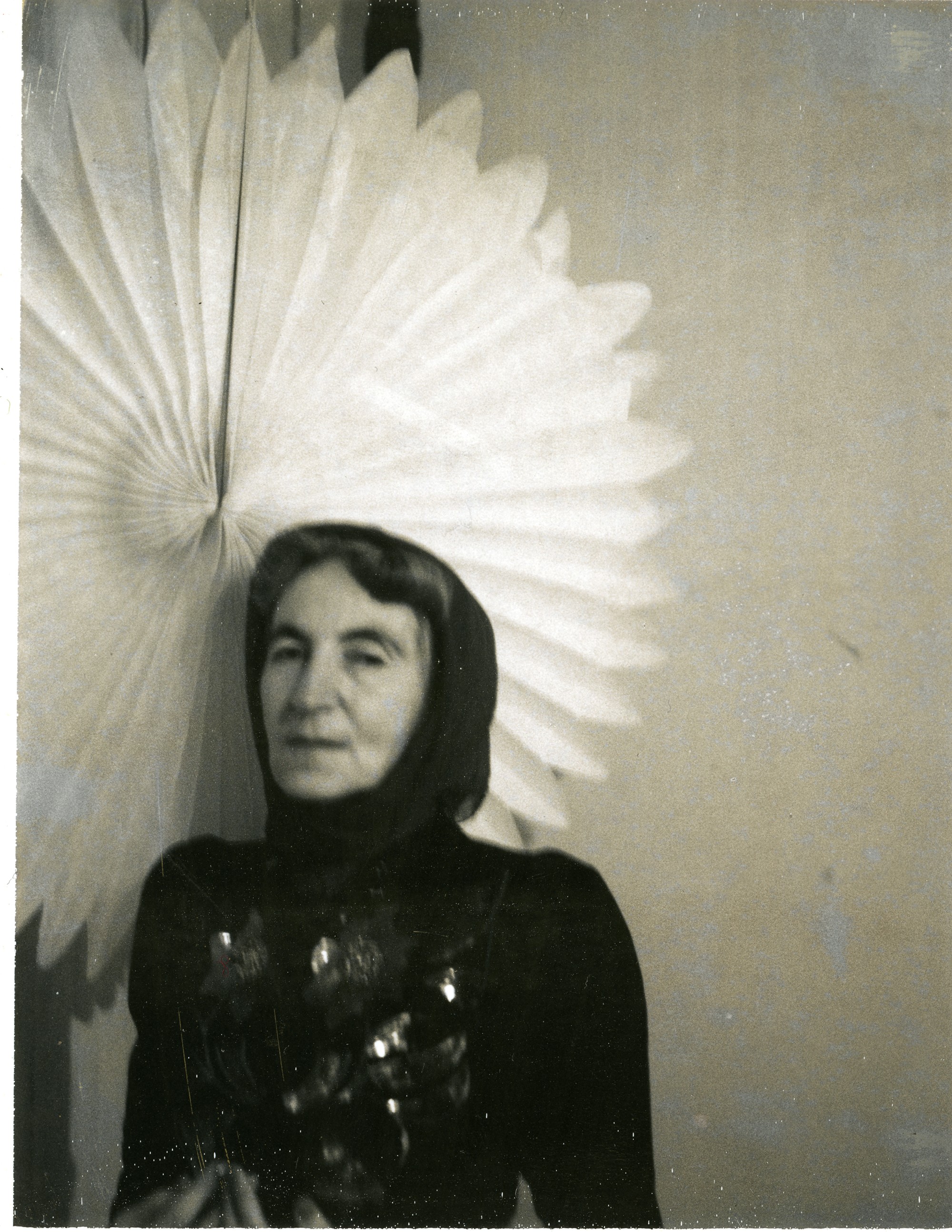 Helen Adam stands in a sparkling top and a head wrap, with a large white fan behind her.