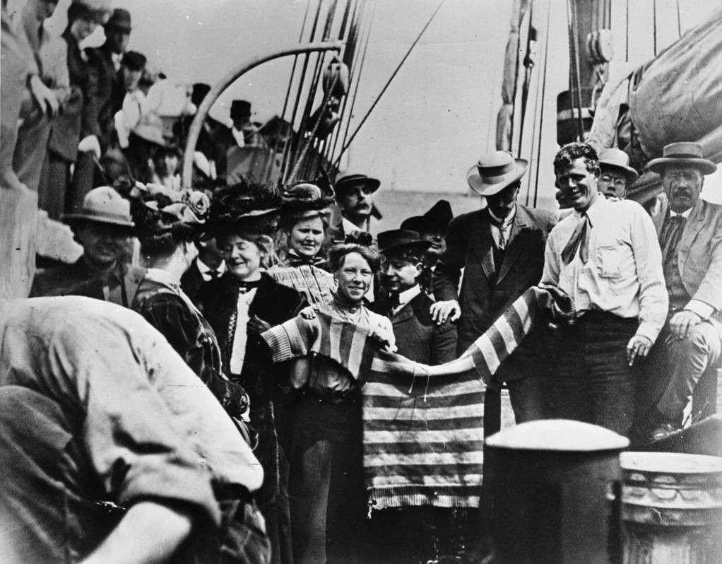 Black and white image of the writer Jack London and his wife, Charmian, on a ship holding out a college sweater, which was flown as a farewell gesture.