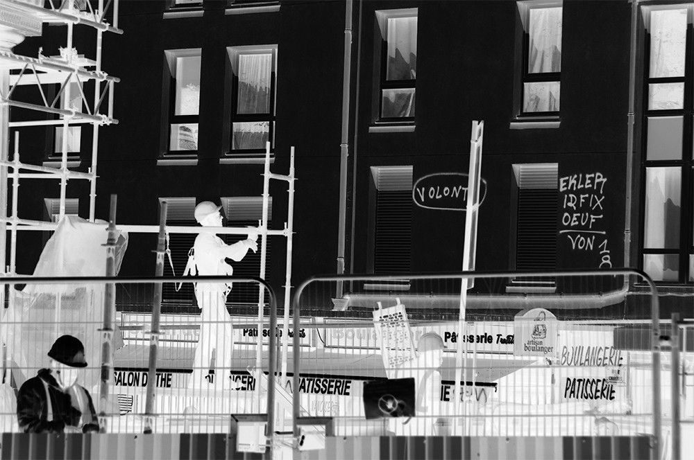 Photographic negative of graffiti on building with construction workers.