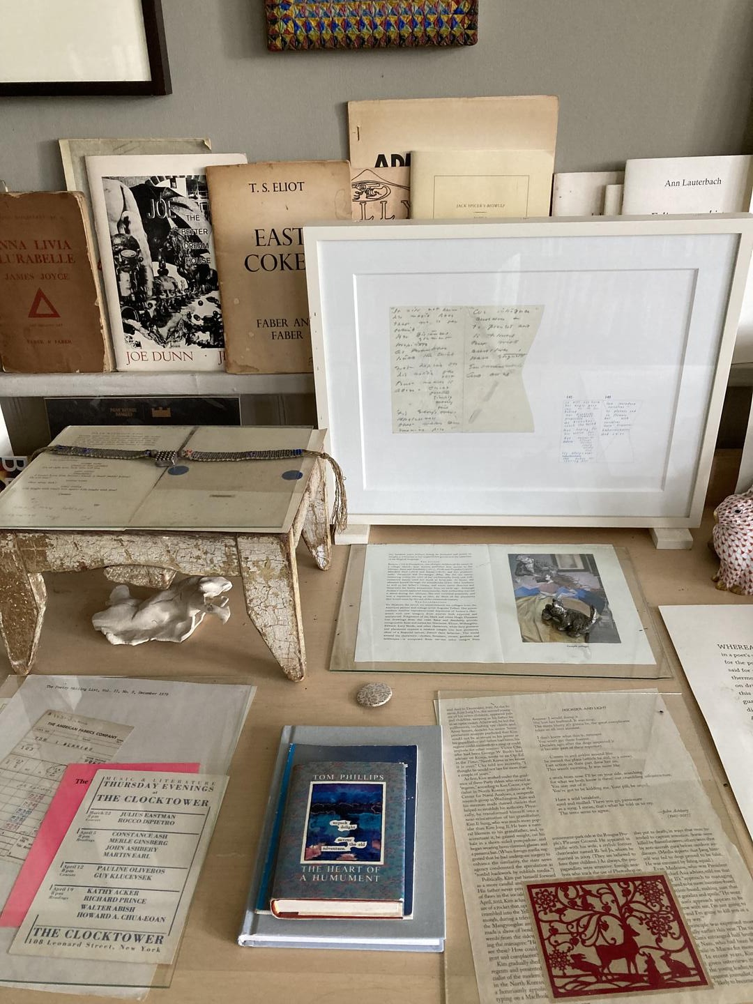 Color photo: A shelf in the background with books facing outward and a table with documents and books 