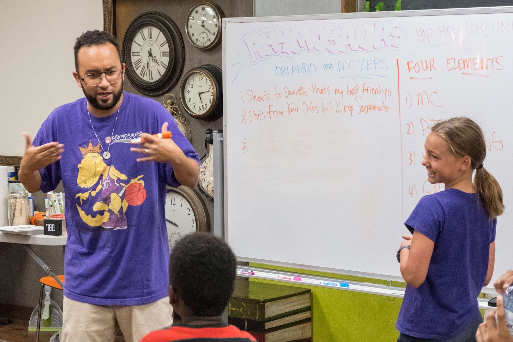 Guest teaching artist stands in front of a whiteboard with tips for spoken word poetry presentation. A smiling student stands next to him.