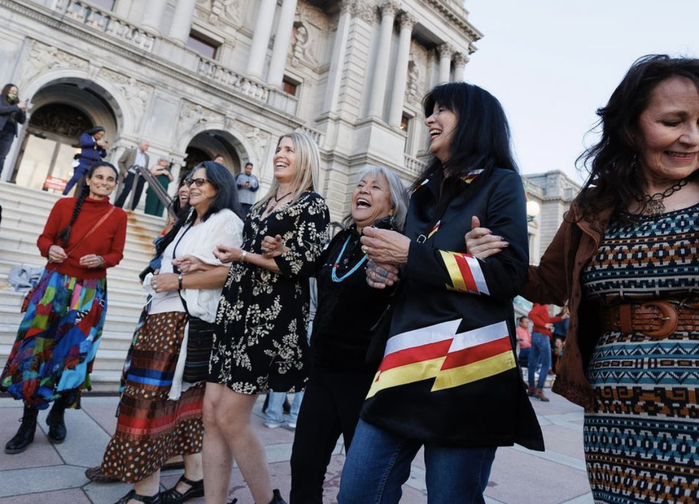 Indigenous poets with Joy Harjo dancing and laughing in front of a stately building in Washington, DC