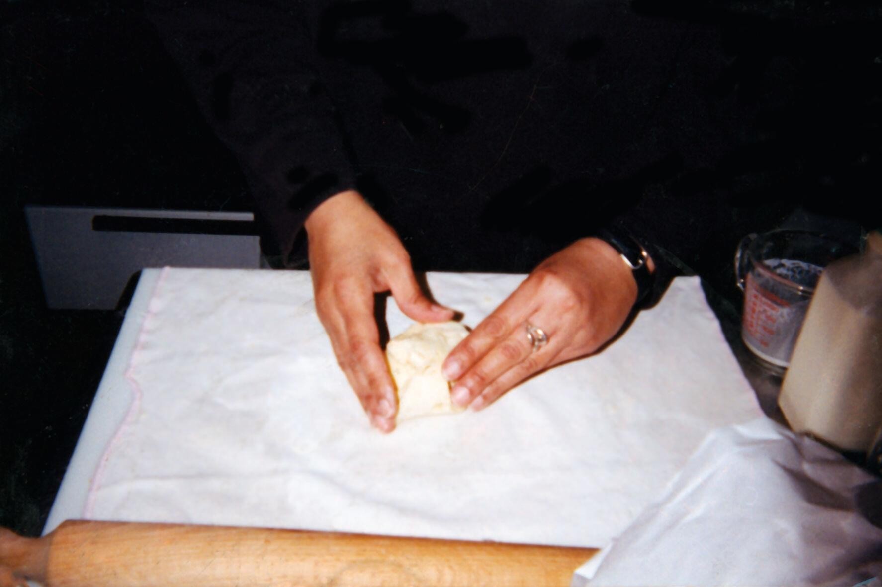 A photograph of hands kneading a small ball of dough on a cloth with a rolling pin in front