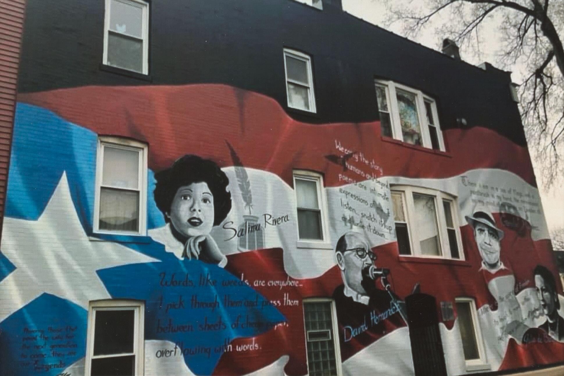 A mural on the side of a three story building with four black and white faces with quotes near each atop a Puerto Rican flag
