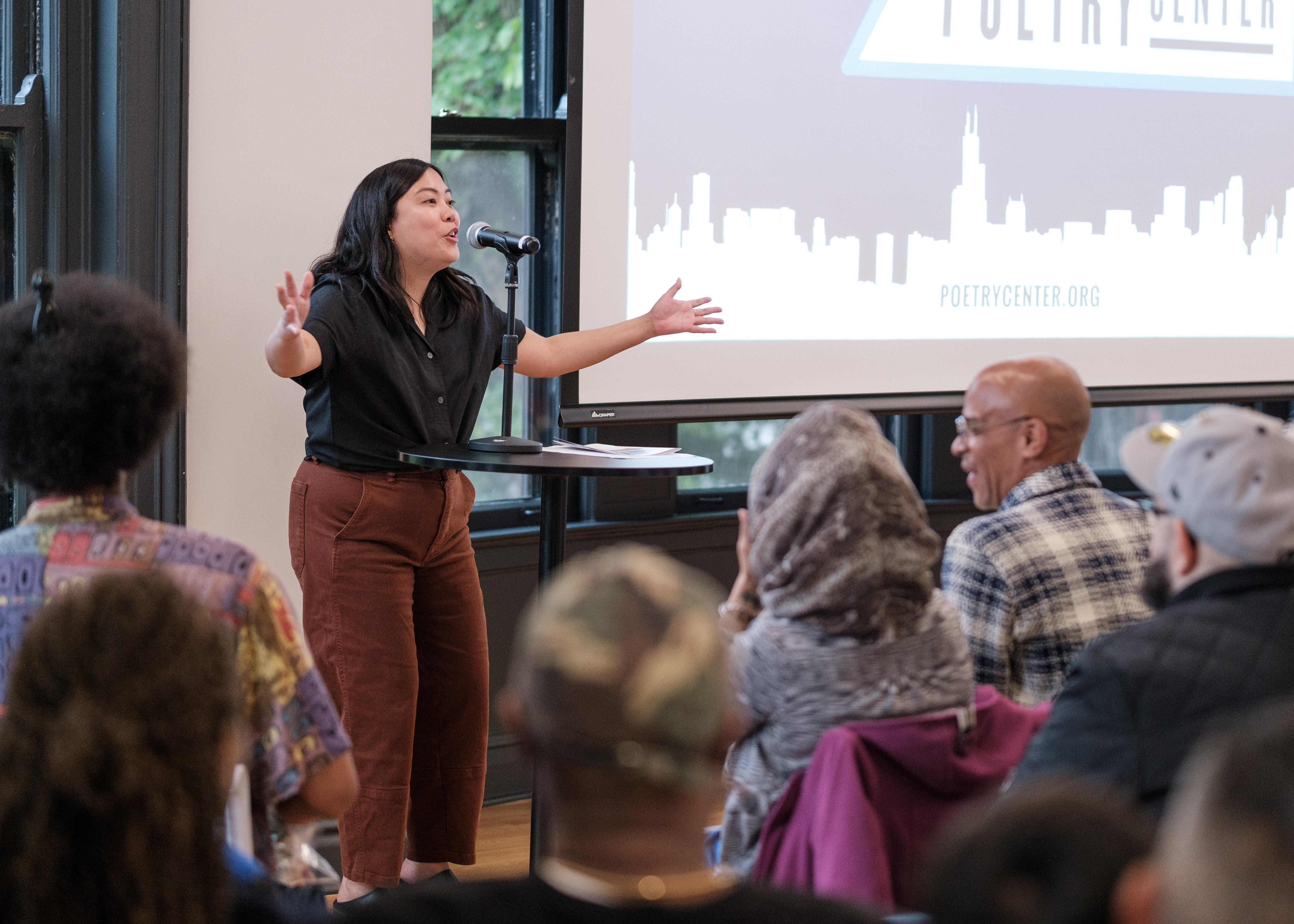 Helene Achanzar, the Director of Programs, enthusiastically speaks to a crowd with her arms outstretched.