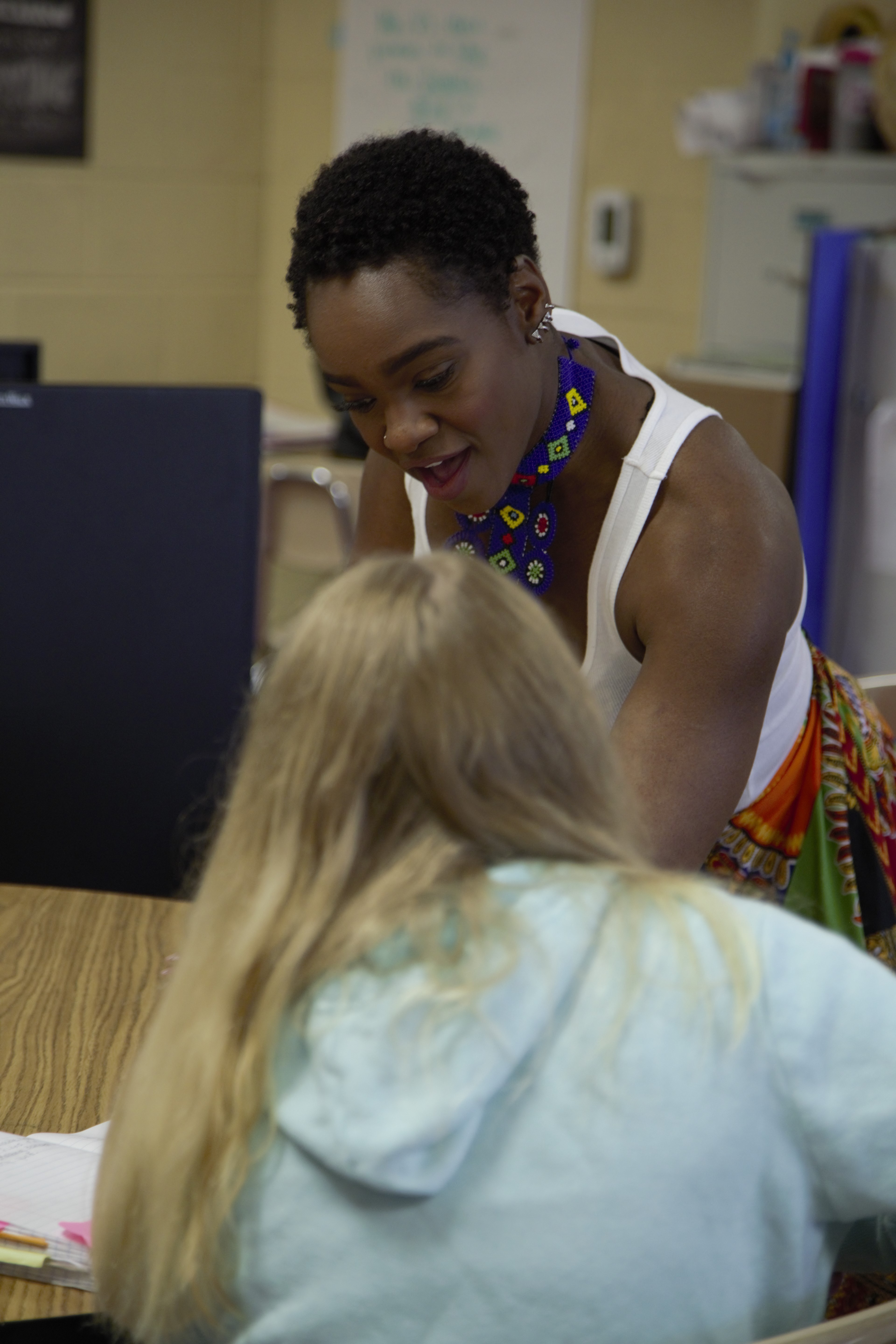 Adult woman leaning over a table with a student who is seen from behind.