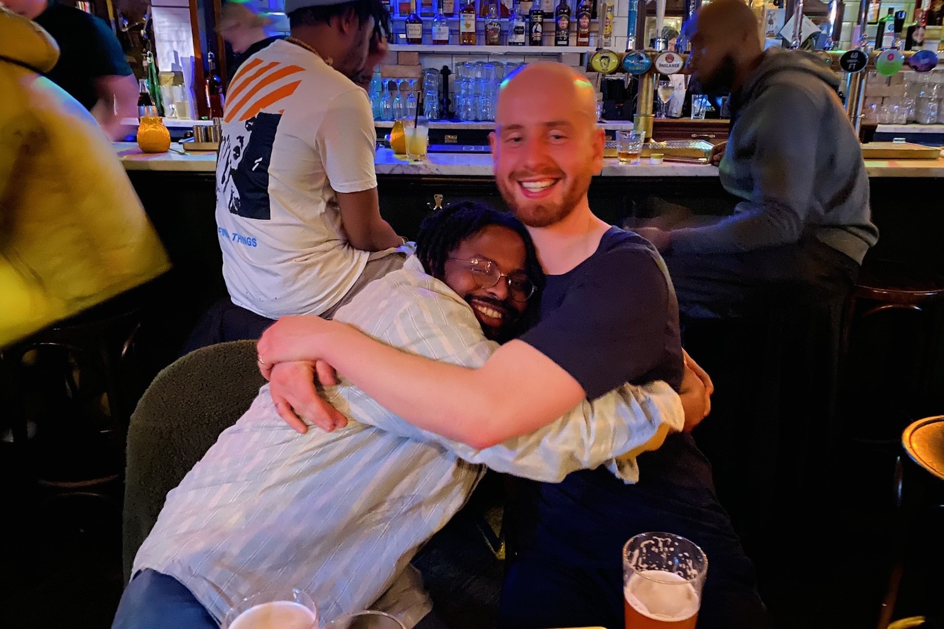 Photo of Gboyega Odubanjo and Joe Carrick-Varty hugging in a pub