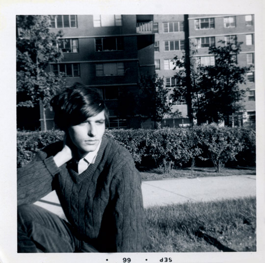 Portrait of Lewis Warsh sitting on the grass in front of a large building.