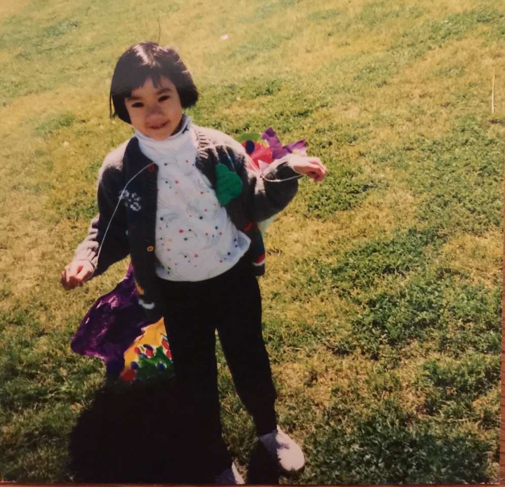 Diana Khoi Nguyen at seven years old, holding a kite, on a strip of lawn.