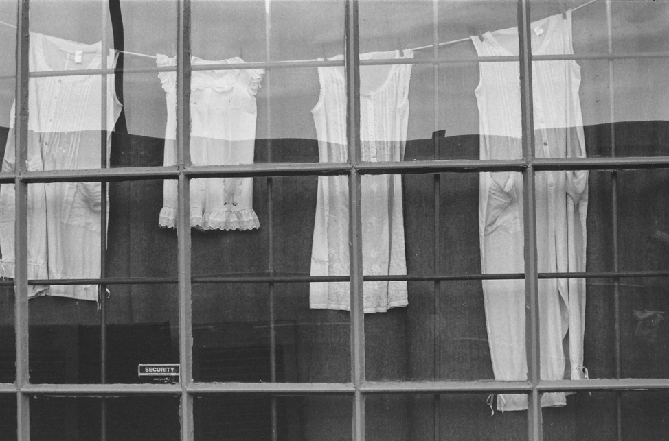 Black and white photo of a window with nightgowns hanging on a line behind.