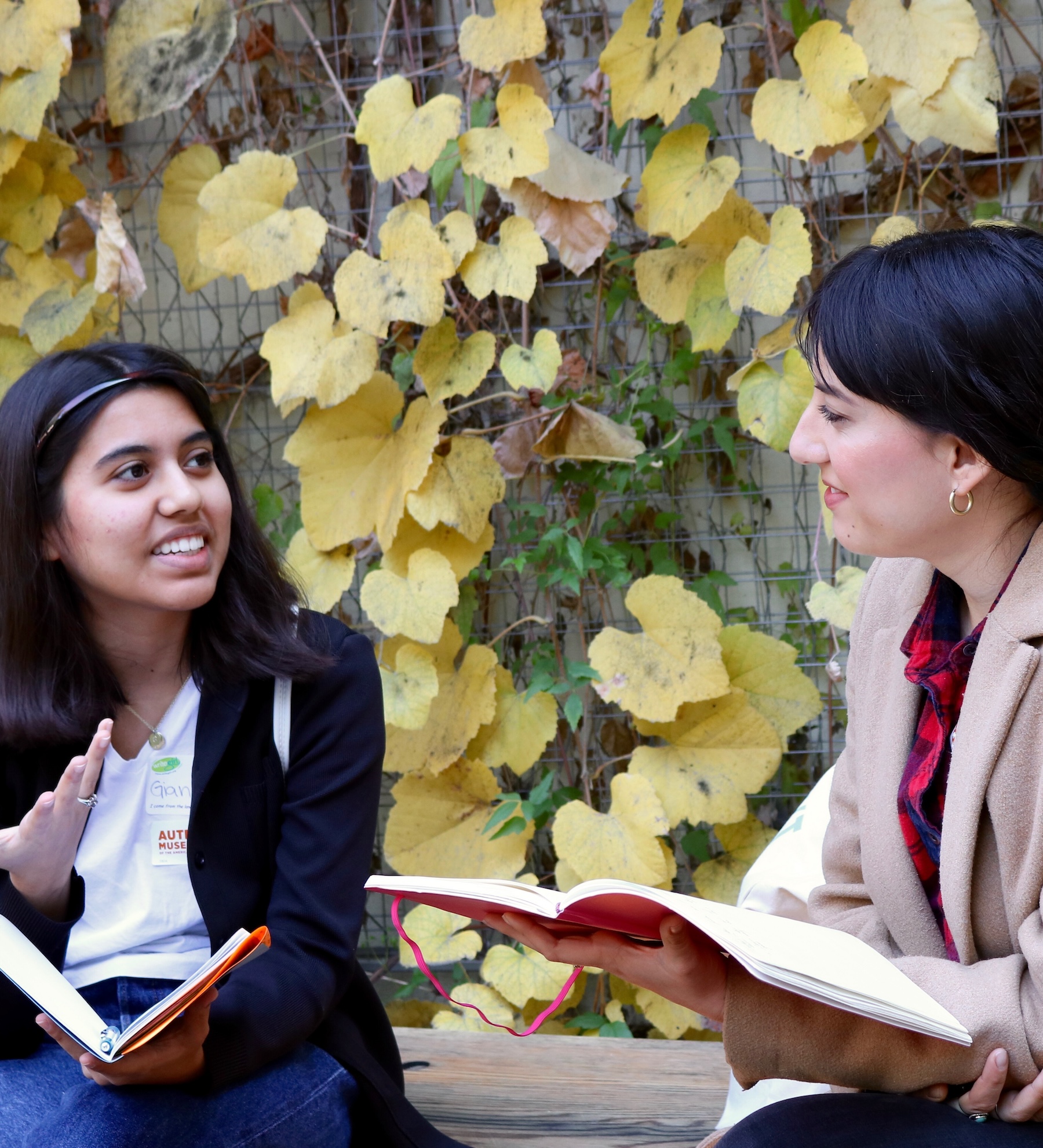 Teen girl and woman holding books in front of an ivied wall